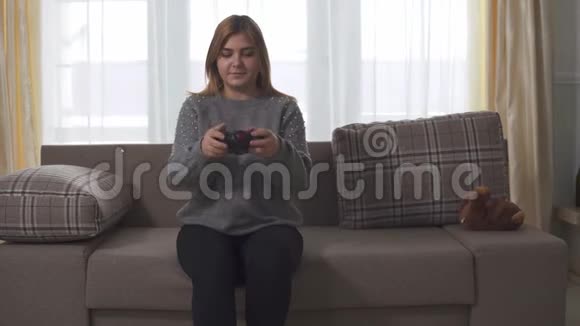 肖像加上大小可爱的女孩在家里坐在沙发上玩电子游戏胖女人手里拿着操纵杆休闲视频的预览图