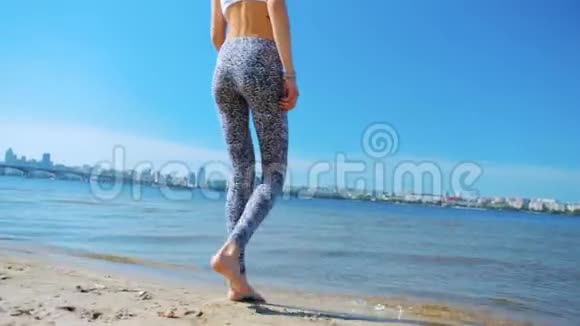 在阳光明媚的早晨美丽的年轻苗条运动女子在沙滩上散步视频的预览图