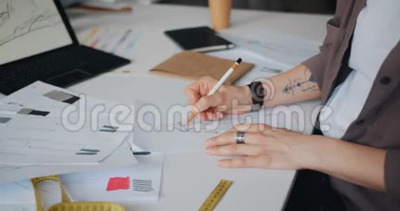 女设计师在桌上纸上绘制服装草图的特写视频的预览图