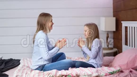 全镜头休闲妈妈和可爱的小毛孩坐在床上享受着愚蠢的拍手视频的预览图