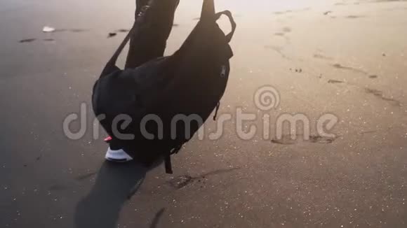 穿着时尚运动鞋的男人在黑色闪亮的沙子上行走他手里拿着背包视频的预览图