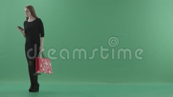 漂亮的有兴趣的女人穿着小黑裙子摆着购物袋她站在演播室里反对视频的预览图