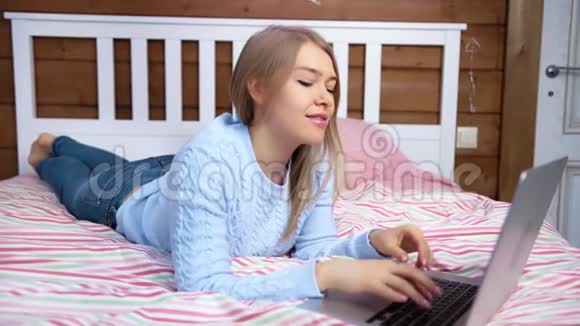 一位爱玩的自由职业者年轻女子微笑着用键盘打字躺在卧室的床上视频的预览图