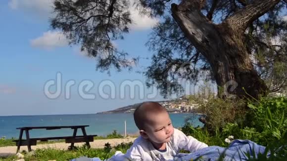 可爱的4个月大的小男孩在树下有肚子花在前面海在背景视频的预览图