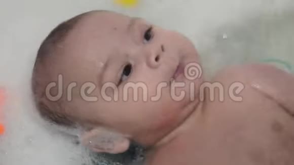 可爱的4个月大的男孩躺在浴缸里泡沫和快速移动视频的预览图