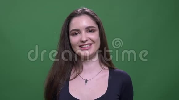 年轻漂亮的深色头发的女性特写镜头欢快地微笑着看着镜头背景是绿色的视频的预览图