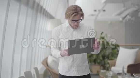 金发快乐的男人戴着眼镜在一间轻松舒适的办公室里跳舞手里拿着小玩意老板关上了上网本视频的预览图