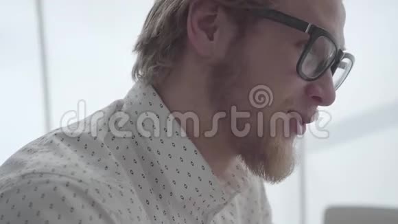 一个戴眼镜的留着胡子的商人坐在一间光线舒适的办公室里英俊的商人在工作侧面视频的预览图