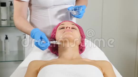 护肤理念美容院的年轻女子美容师向女性客户应用面膜水疗中心女性接受者视频的预览图