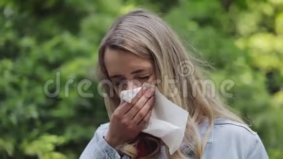 有过敏症状的年轻女子站在公园里吹鼻子生病的女孩打喷嚏把她的鼻子视频的预览图