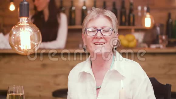 一位美丽的老太太坐在酒吧里的一张桌子上和摄像机说话的肖像视频的预览图