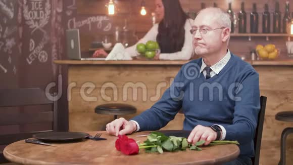 一位悲伤的老人坐在餐厅的桌子旁等待他的约会视频的预览图