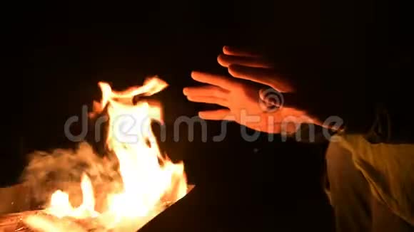 一个人在完全的黑暗中把手放在明火上取暖男人夜晚的炉火旁视频的预览图