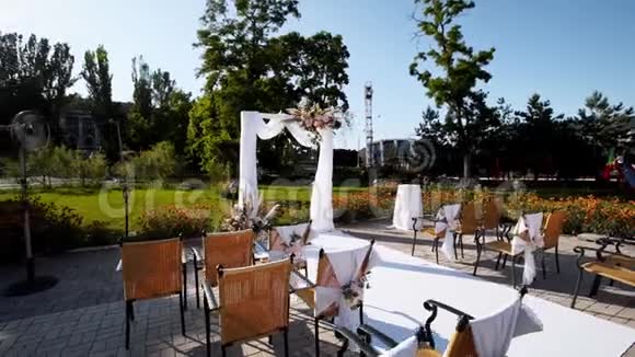 在阳光明媚的夏日婚礼拱门装饰着鲜花节日花装饰在椅子上玫瑰和羽毛视频的预览图