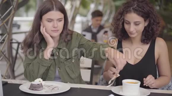 两个年轻女朋友坐在户外咖啡馆里吃蛋糕的肖像年轻女孩一起享用美食视频的预览图