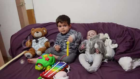 两岁和四个月大的男孩在床上玩木琴和软玩具视频的预览图