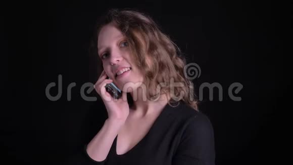 黑色背景下年轻卷发女孩在智能手机上愉快交谈的肖像视频的预览图