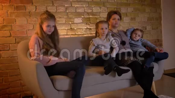 白种人的母亲和三个女儿坐在一起在舒适的家里笑着看电影视频的预览图