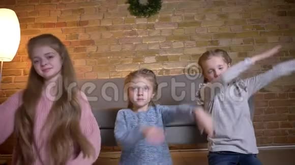 三个小白种人女孩坐在地板上的肖像在舒适的家中对着镜头示意成功的迹象视频的预览图