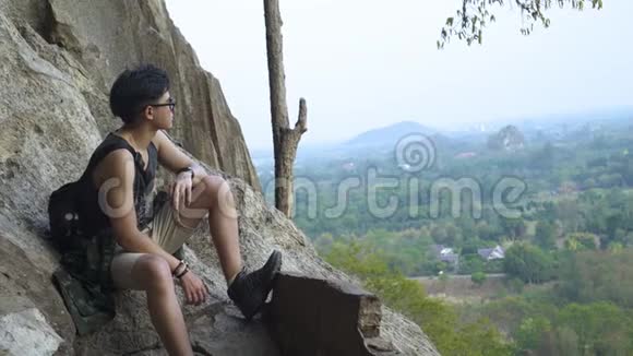 坐在悬崖边的亚洲帅哥从高处俯瞰美景视频的预览图