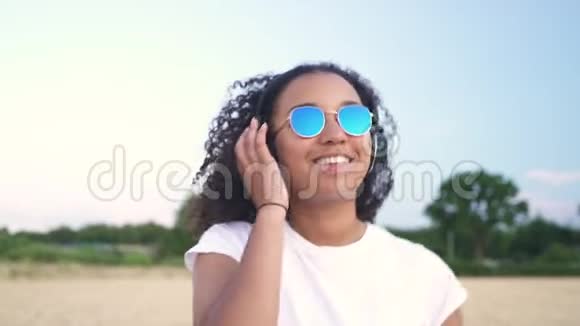 穿着白色T恤和蓝色太阳镜走路听无线耳机音乐的非洲裔美国少女少女视频的预览图