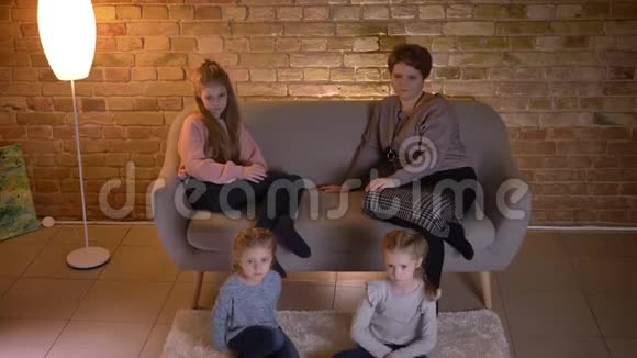 高加索母亲带着三个女儿坐在沙发上在温馨的家庭氛围中聚精会神地看电影视频的预览图