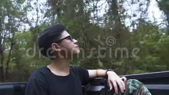 漂亮的亚洲男人坐在皮卡车的后面用纯净的森林空气提神视频的预览图
