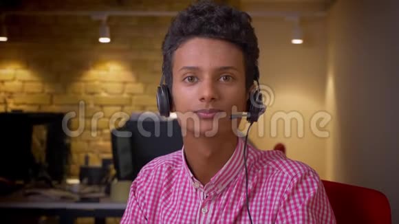 印度年轻商人戴着耳机在办公室室内看摄像机的特写镜头视频的预览图