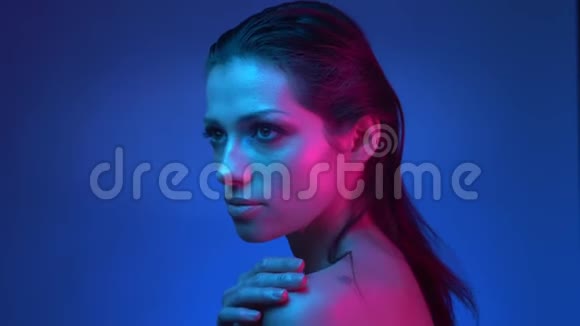 闪闪发光的模特用蓝色和粉红色的霓虹灯照着相机温柔地抚摸着她的肩膀视频的预览图