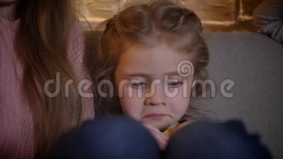 在舒适的家庭背景下小白种人女孩坐在沙发上吃饼干的特写肖像视频的预览图