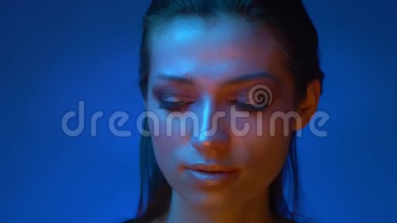 未来派的模特在蓝色的霓虹灯中闪耀着闪亮的妆容她的眼睛从左到右神秘地进入视频的预览图