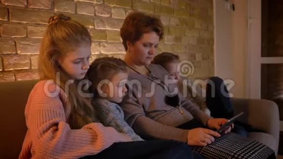 特写家庭肖像描绘了白种人的母亲和女儿观看平板电脑对舒适感兴趣视频的预览图