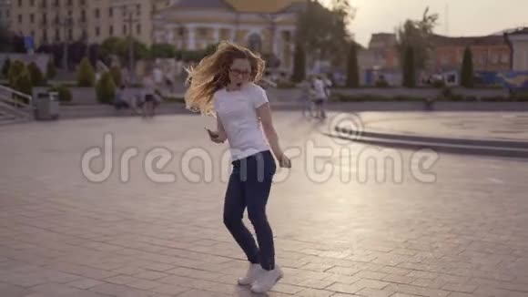 有趣的金发女郎在街上玩得很开心一个女孩手里拿着手机跳舞和大笑4K视频的预览图