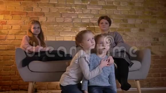白种人母亲的家庭肖像三个女儿拥抱在一起在舒适的家庭氛围中看电影视频的预览图