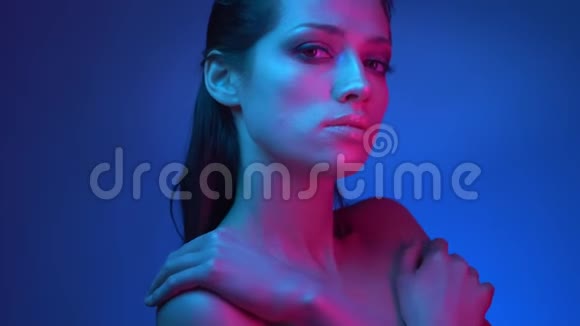 闪烁的时尚明星穿着蓝色和粉红色的霓虹灯摆在相机上她的双手交叉在工作室的胸部视频的预览图