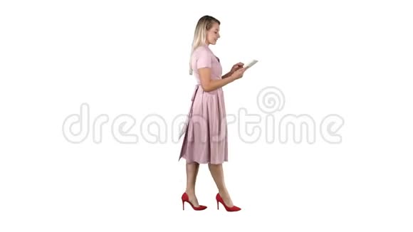 金发碧眼穿着粉色连衣裙走路在白色背景上使用平板电脑视频的预览图