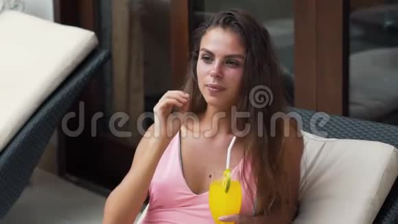 穿着泳衣的女孩正在躺椅上休息喝着鸡尾酒微笑着慢动作视频的预览图