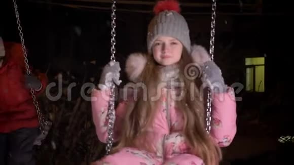 在冬天的街道背景下小漂亮女孩慢慢地骑在秋千上平静地微笑着进入镜头的肖像视频的预览图
