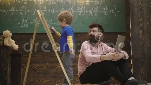 男孩在黑板上用粉笔写字可爱的蹒跚学步的男孩在木制背景上画黑板人控制学习视频的预览图