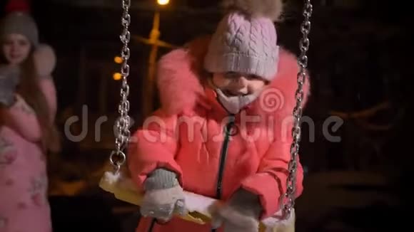 特写小女孩穿着红色外套在秋千上的肖像在冬天的街道背景下快乐地看着镜头视频的预览图