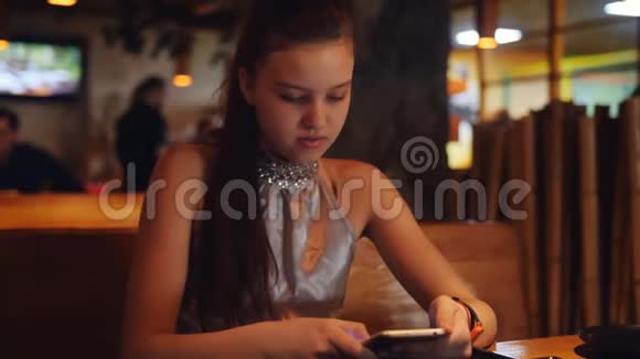 一个十几岁的女孩在餐厅的餐桌上使用智能手机以期待订单视频的预览图