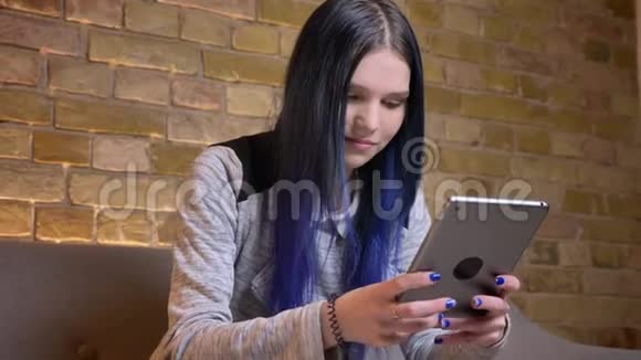 一位年轻漂亮的白种人潮女的特写镜头她染着头发在平板电脑上发短信在舒适的环境中微笑视频的预览图