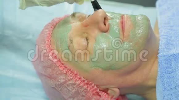 一位女性美容师用刷子把泥面具涂在男人的脸上侧视图视频的预览图