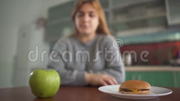 此外坐在模糊背景下的大小女孩认为她应该吃美味的汉堡包或多汁的绿色苹果视频的预览图
