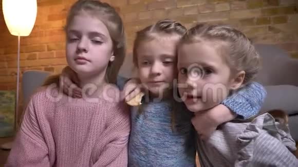 三个小白种人女孩拥抱在一起在舒适的家庭氛围中落在地板上的肖像视频的预览图