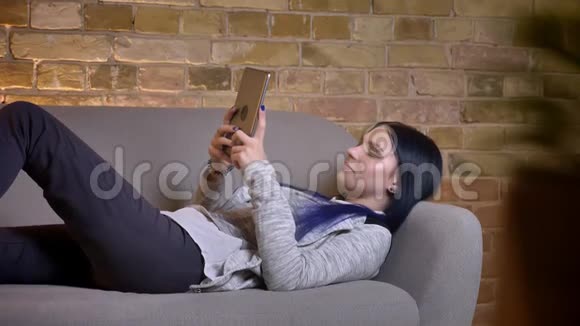 年轻漂亮的白种人女性在平板电脑上打字躺在平板电脑上时微笑着放松视频的预览图