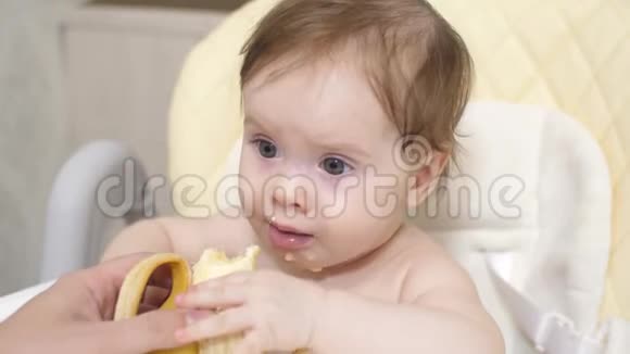 妈妈用香蕉喂小孩婴儿在他的孩子椅子上吃早餐美丽的小家伙吃香蕉视频的预览图