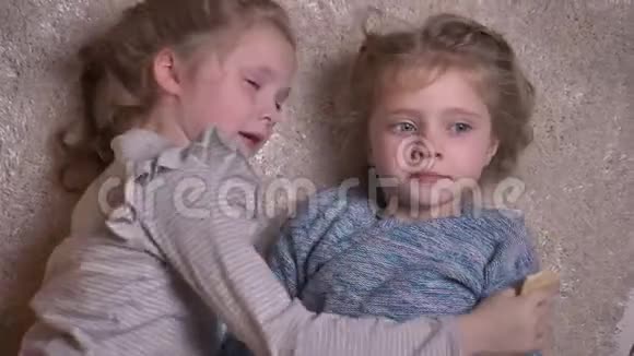 两个有趣的小女孩在地板上相互拥抱和亲吻的顶级肖像视频的预览图