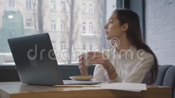 美丽的女人想着看着窗外手里拿着咖啡杯紧紧地抱着很漂亮的女人享受着视频的预览图