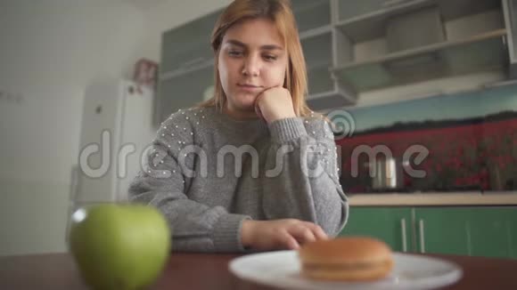 把苹果和汉堡放在胖女孩面前年轻女子先吃汉堡包然后把它放在视频的预览图